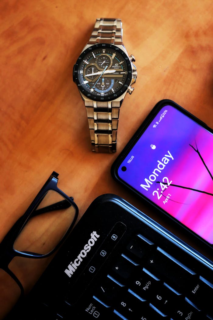 Home Flat lay of a watch, smartphone, glasses, and keyboard on a desk.